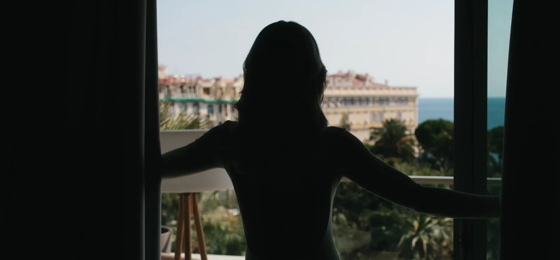 Silhouette ouvrant les rideaux de sa suite sur la mer